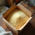 Boîte de couscous périmée ouverte sur une table en bois, grains agglomérés et décolorés montrant des signes de détérioration