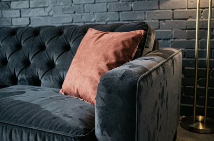 Détail de canapé d'angle en velours anthracite avec coussin terracotta et coutures apparentes dans un appartement urbain