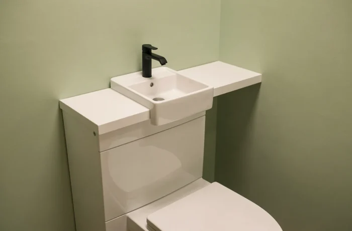 Lave-mains en céramique blanche intégré au-dessus du coffrage de bâti-support avec robinet mural noir mat dans des toilettes peintes en vert sauge