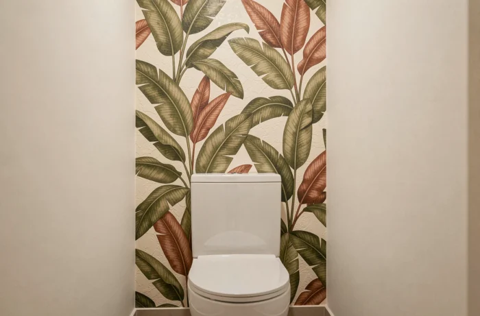 Papier peint vinyle expansé à motifs botaniques en olive et terracotta posé sur un seul pan mural derrière la cuvette suspendue dans de petites toilettes