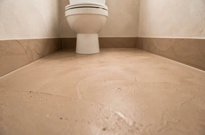 Sol en résine microcement sans joint ton sable beige posé de mur à mur avec remontée intégrée en plinthe continue dans de petites toilettes suspendues